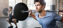 Man squats with a barbell in a gym.